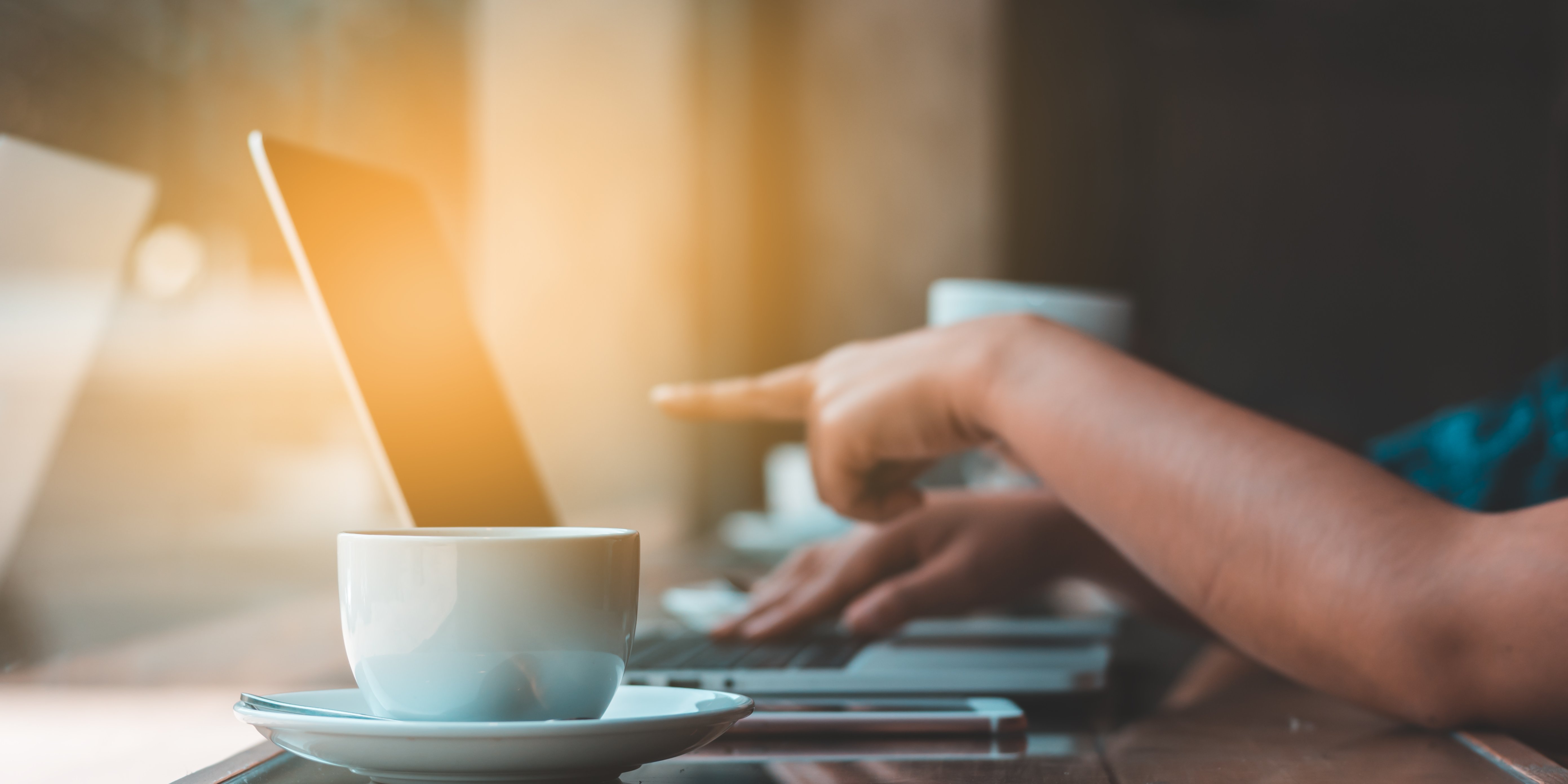 Tasse an Laptop mit Hand die auf Bildschirm zeigt