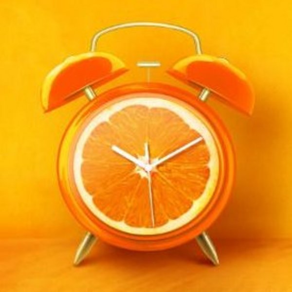 Eine Orange als Wecker vor orangefarbenem Hintergrund